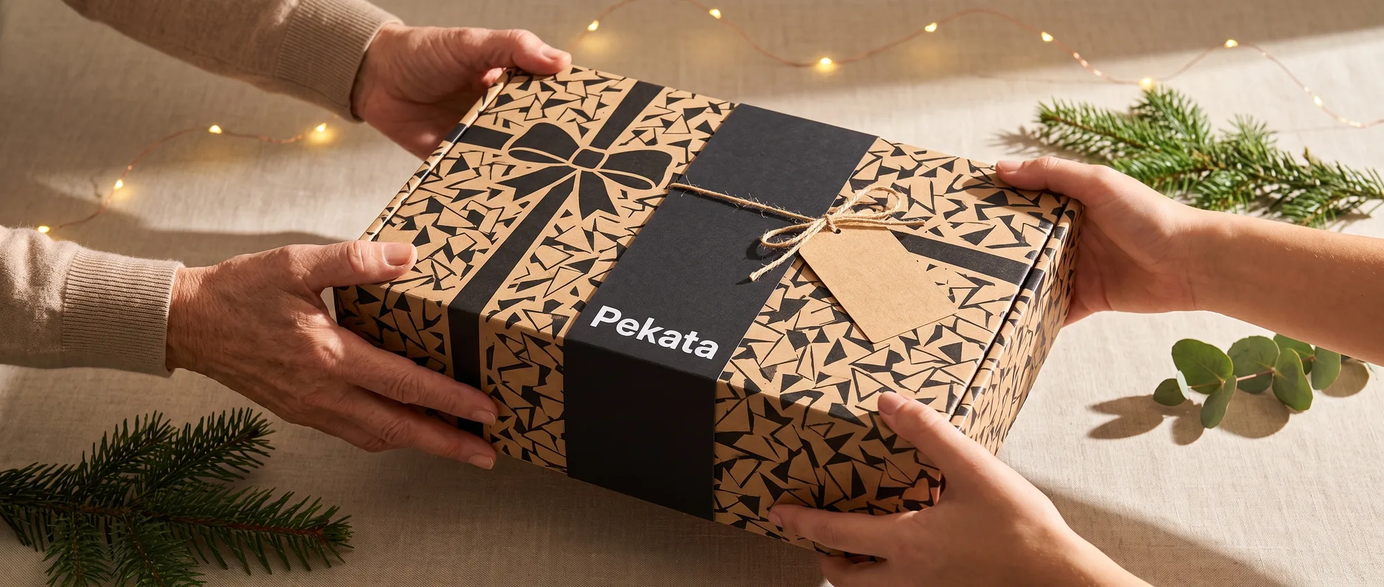 Deux paires de mains offrant et recevant une boîte cadeau Pekata avec étiquette kraft et motif trencadís